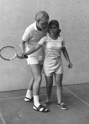 A girl is guided in swinging a tennis racket