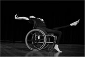 A woman who uses a wheelchair dances across the stage with her arms and legs outstretched.