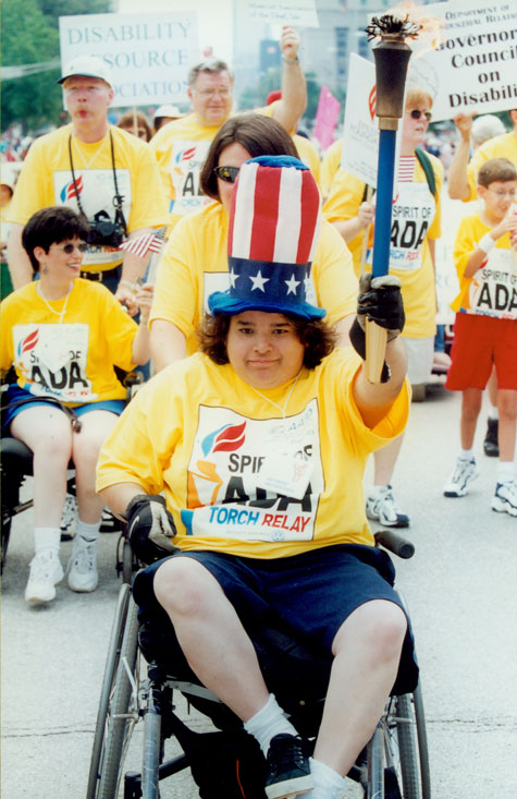 Ana Jennings, a wheelchair user, rides through the street holding a torch.